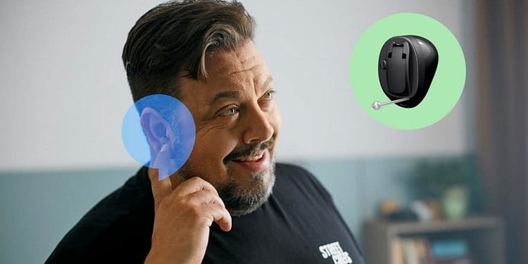 Personne avec un doigt sur l'oreille montrant son appareil auditif invisible
