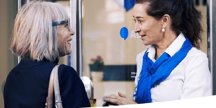 Accueil chaleureux d’une cliente par un audioprothésiste Audika devant un centre de soins auditifs.
