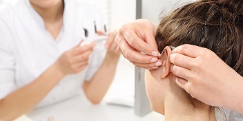 femme posant un appareil auditif sur une jeune fille