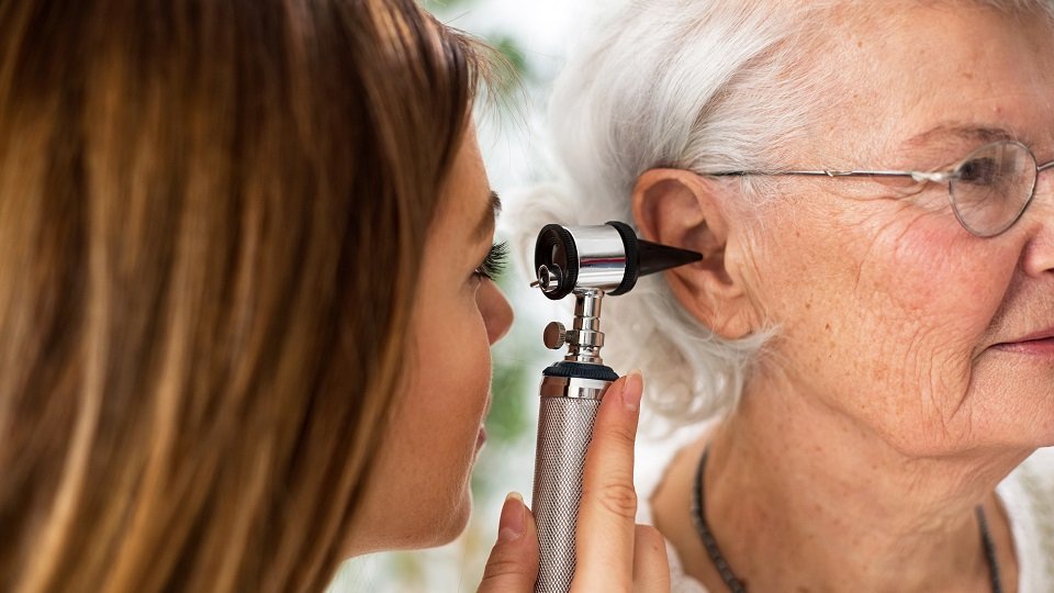 Une audioprothésiste examine l’oreille d’une femme âgée avec un otoscope pour évaluer le besoin d’un nettoyage auditif.