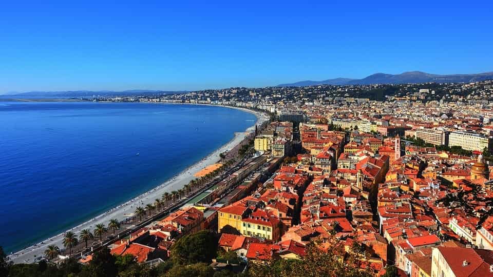 Ville de Nice avec sa promenade en bord de mer, ses toits rouges et ses collines en arrière-plan.