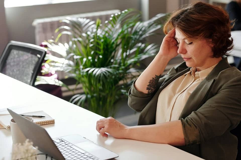 Une femme au travail se tient la tête car elle souffre d'acouphènes