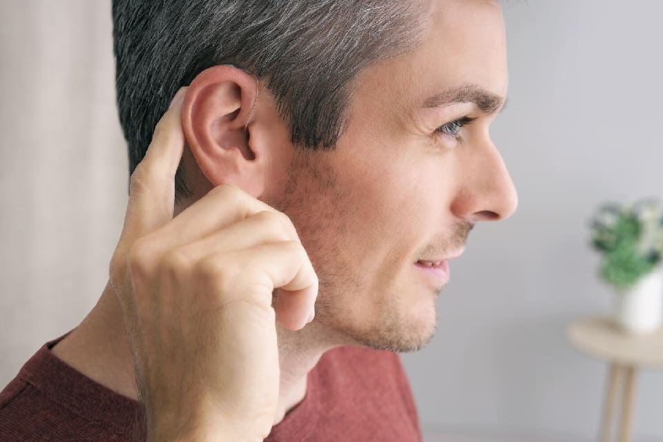 Appareil auditif discret porté derrière l’oreille d’un homme, avec un doigt pointant vers l’appareil.