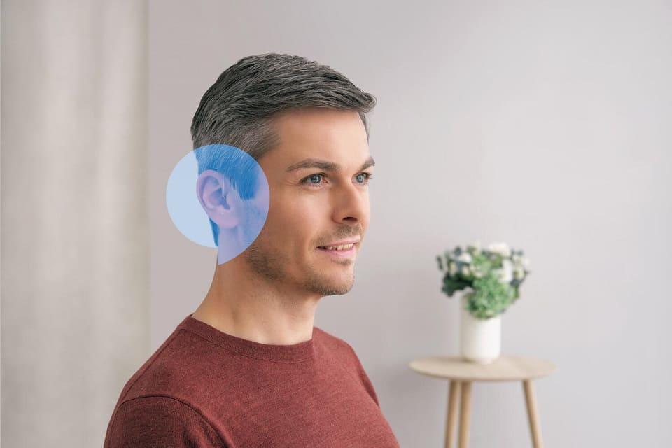 Homme portant des aides auditives Audika avec arrière-plan moderne et lumineux
