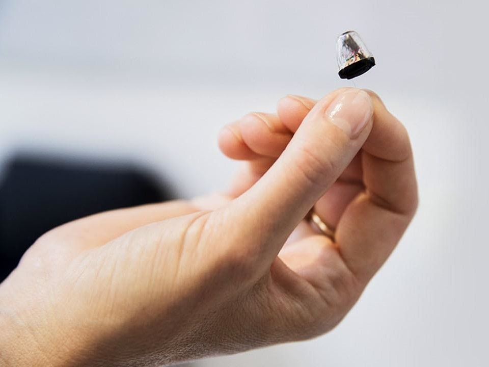 Une main présente un appareil auditif intra-auriculaire