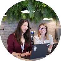 Deux femmes travaillant sur des ordinateurs portables dans un espace moderne avec une décoration végétale en arrière-plan.