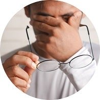 Un homme tenant des lunettes et se couvrant les yeux, illustrant l’inconfort visuel associé à des troubles comme le nystagmus.