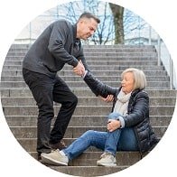 Homme aidant une femme âgée tombée dans les escaliers, illustrant des problèmes de perte d’équilibre.