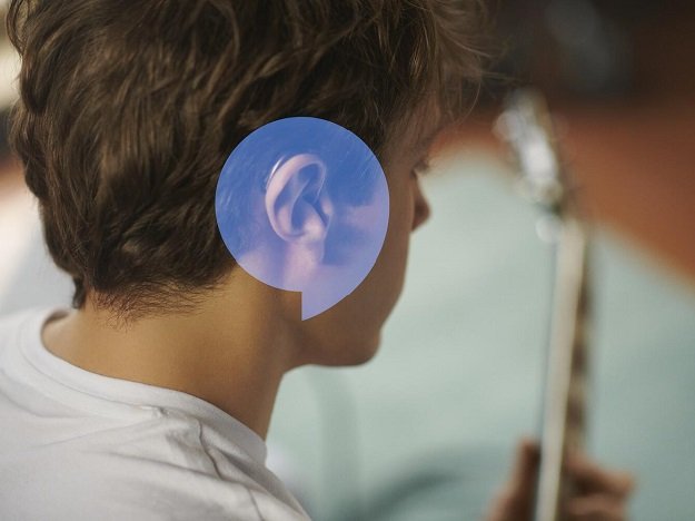 Un adolescent portant un appareil auditif et jouant de la guitare sur son lit.