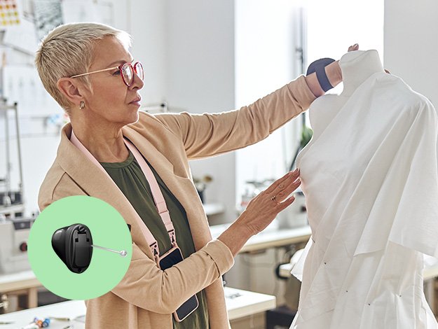 Styliste utilisant de petits appareils auditifs Audika dans un atelier de couture