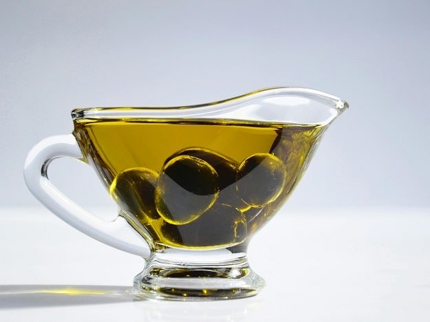 Tasse en verre transparente remplie d’huile d’olive dorée et d’olives noires