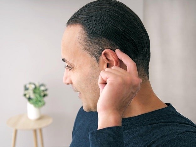 Une personne insère un appareil auditif derrière son oreille.