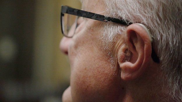 Vue rapprochée du profil d’un homme âgé portant un appareil auditif Audikafull et des lunettes.