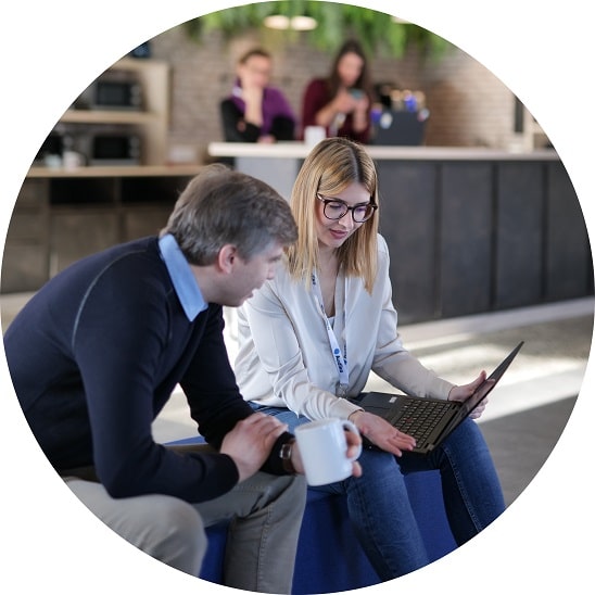 Une employée Audika explique des informations à un homme tout en lui montrant quelque chose sur un ordinateur portable dans un espace convivial.