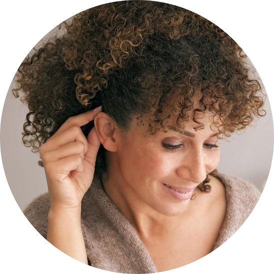 Une femme aux cheveux bouclés ajuste un appareil auditif.