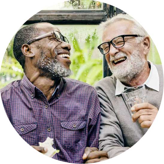 Deux hommes partagent un moment de convivialité en riant lors d’un repas.