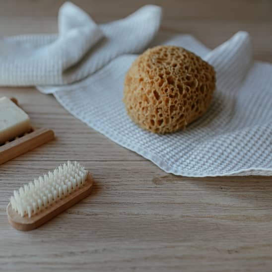 Brosse, éponge naturelle et serviette blanche sur une surface en bois, utilisés pour l'hygiène des oreilles