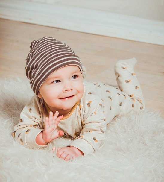 Un bébé allongé sur un tapis doux, habillé avec une tenue à motifs et un bonnet rayé.