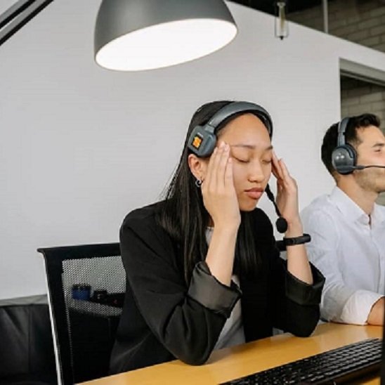 Une femme portant un casque au travail se tient la tête, signe de gêne liée aux acouphènes.