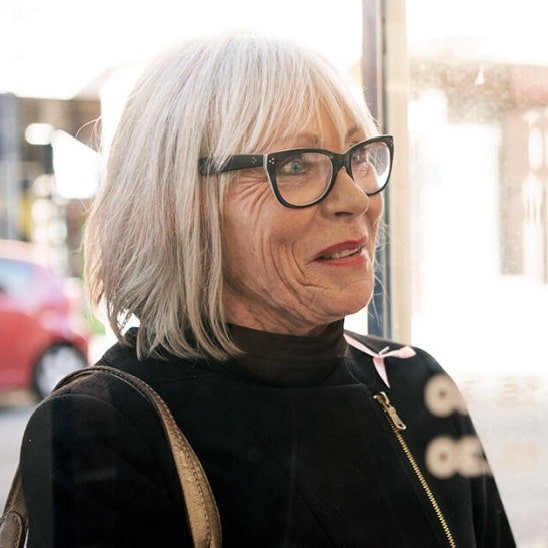 Une femme aux cheveux gris entre dans un centre Audika pour consulter un audioprothésiste.