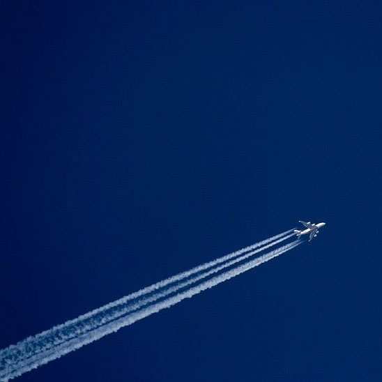 Un avion vole à haute altitude, laissant derrière lui deux traînées de condensation blanches dans un ciel bleu dégagé, évoquant un voyage aérien rapide et silencieux.