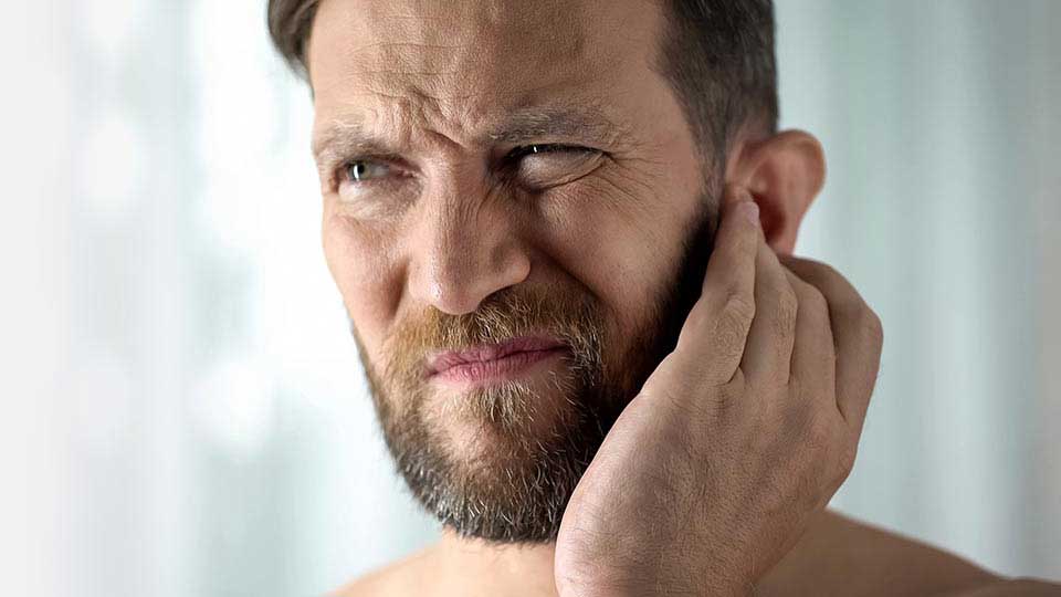 Un uomo tocca il proprio orecchio con una mano, suggerendo un possibile disagio o perdita uditiva. Sfondo sfocato e luminoso. 