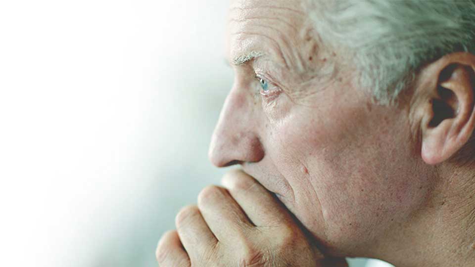 Un orecchio umano con capelli grigi visibili sul lato destro, inquadrato da vicino. Sfondo bianco e verde chiaro sfocato.