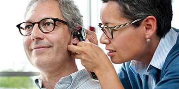 Un audioprotesista controlla l’orecchio di una persona con un otoscopio in una clinica per l’udito. La scena richiama un test dell’udito in un ambiente professionale.