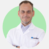 Denis Susana, audioprotesista con camice bianco Audika e sfondo verde