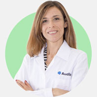 Katia Vinai, audioprotesista presso Audika, con camice bianco e sfondo verde.