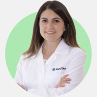 Sara Esposito, audioprotesista presso Audika, con camice bianco e sfondo verde.