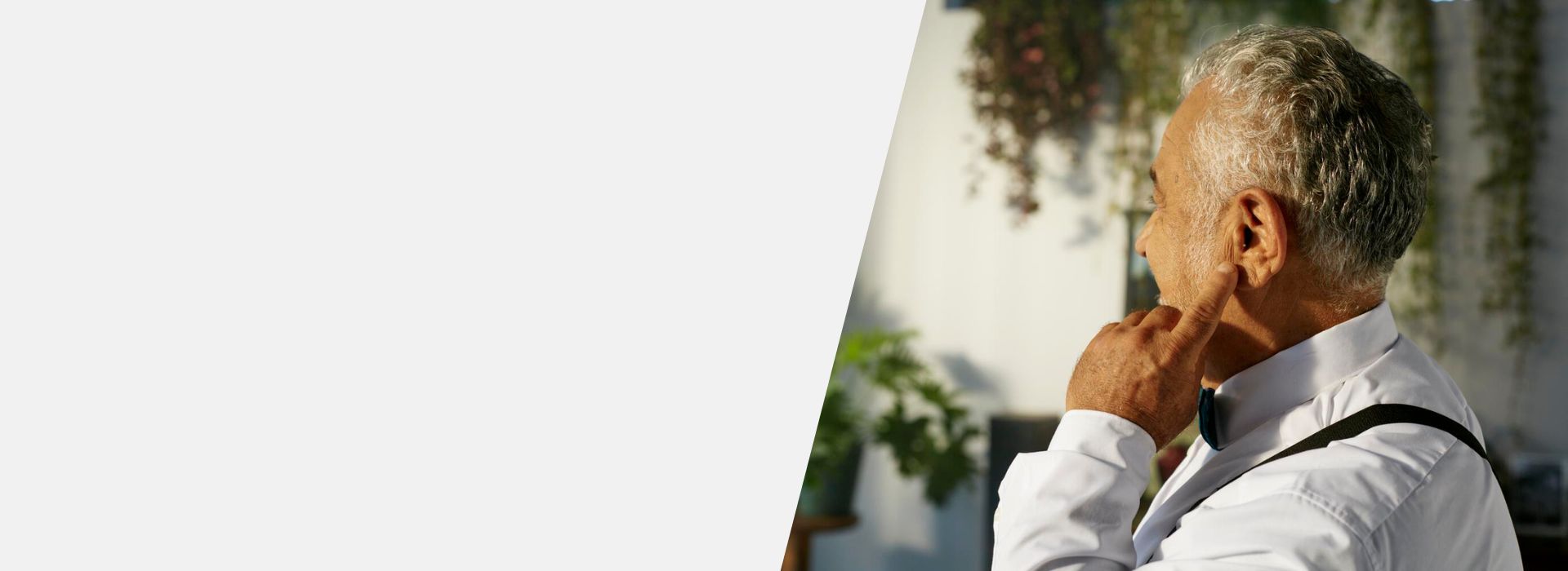 Uomo anziano che tocca l'orecchio destro, sintomo di acufene, in un ambiente luminoso e rilassante.