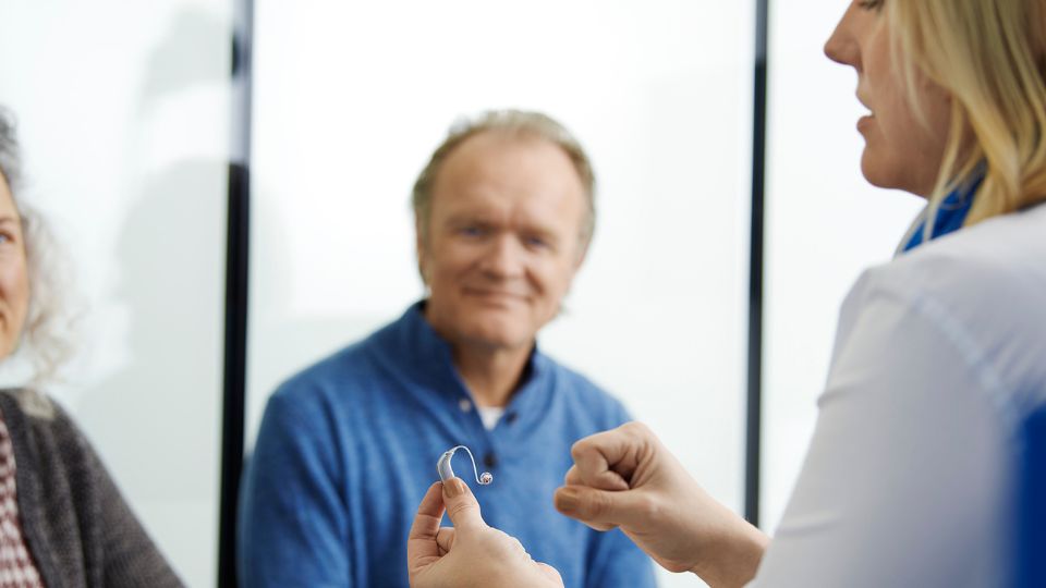 Audioprotesista che mostra un apparecchio acustico a una coppia di pazienti