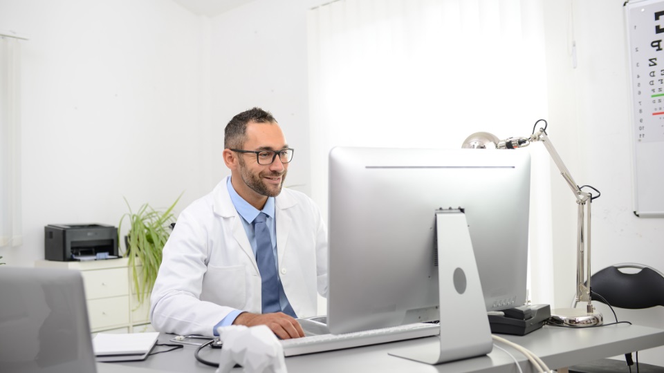 Dottore in camice bianco che lavora al computer in un ufficio moderno di cura dell’udito.