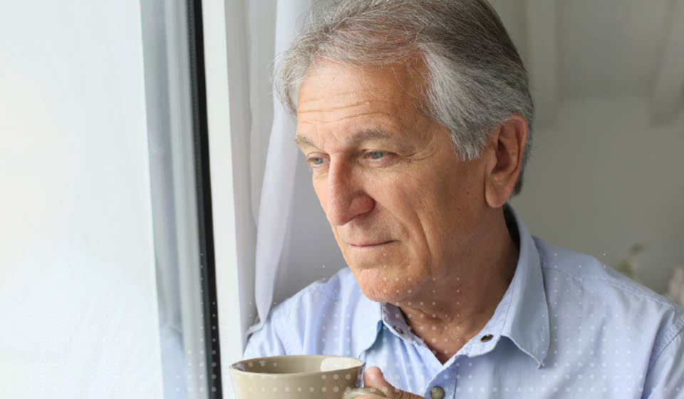 Man ervaart mogelijk beginnend gehoorverlies terwijl hij uit het raam kijkt met een kopje in zijn hand.