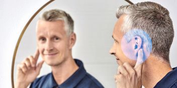 Persoon met gehoorapparaat kijkt glimlachend in de spiegel