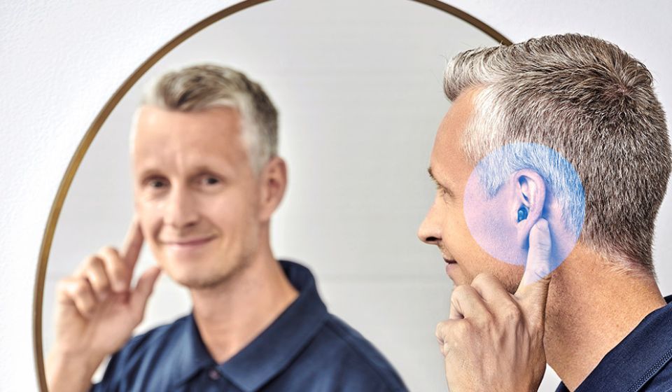 Persoon met gehoorapparaat kijkt glimlachend in de spiegel