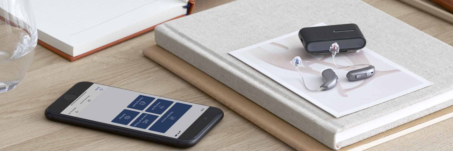 Hoortoestellen met geavanceerde technologie naast smartphone en oplaadcase op houten bureau