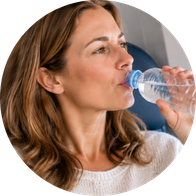 Een mevrouw die in het vliegtuig zit en water aan het drinken is