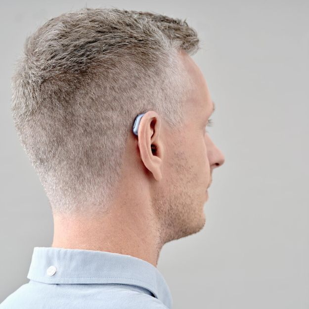 Man met een achter-het-oor gehoorapparaat voor een grijze achtergrond