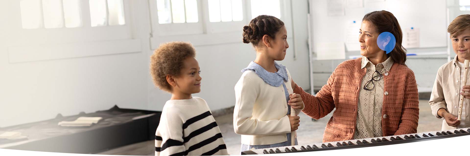 Een jong meisje dat met een groep kinderen en een leraar een muziekinstrument bespeelt, met de nadruk op een zichtbaar gehoorapparaat.