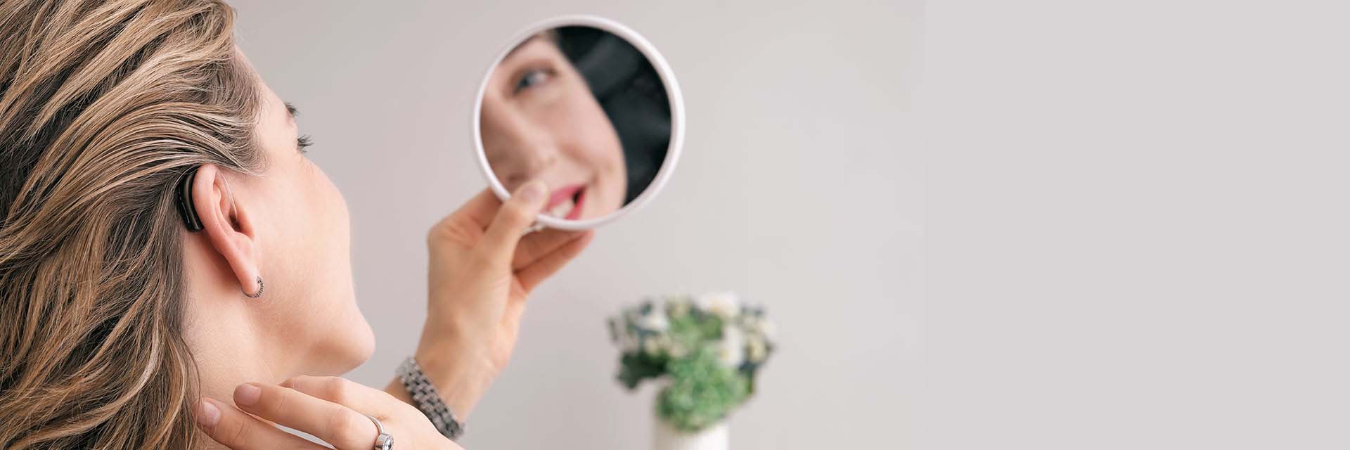 Vrouw past gehoorapparaat aan terwijl ze in een spiegel kijkt