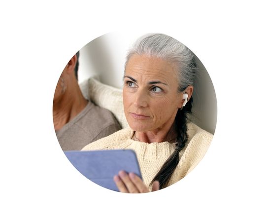 Een mevrouw die thuis op haar tablet met oortjes een hoortest doet