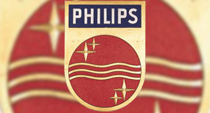 Het beeld toont het Philips-logo, bestaande uit een rode cirkel met sterren en golvende lijnen, omlijst door goud. Bovenaan staat 'PHILIPS' in witte letters op een blauwe achtergrond.