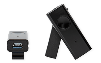 Twee zwarte accessoires lijken gerelateerd aan hoortoestellen, waarschijnlijk voor draadloze audiostreaming of connectiviteit. Links toont een USB-aansluiting, rechts een compact apparaat met knop en microfoon.