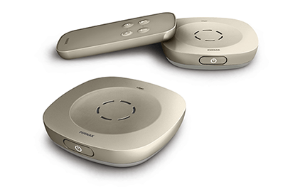 Twee Philips-hoorapparaataccessoires met ronde vormen en aan/uit-knoppen, gecombineerd met een afstandsbediening met vier knoppen, ontworpen voor gehoorondersteuning binnen een moderne context van hoorhulpmiddelen.