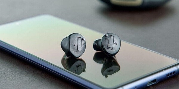 Aparaty słuchowe Oticon Own™ leżące na ekranie smartfona.