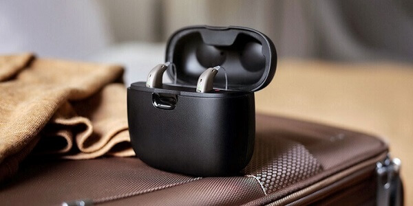 Aparaty słuchowe Oticon Real™ w etui ładującym na walizce.