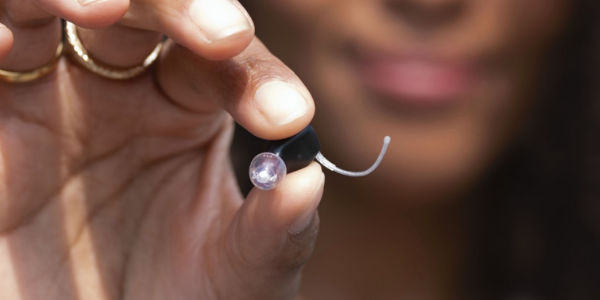 Zadowolony pacjent trzyma aparat słuchowy Oticon Zeal™.