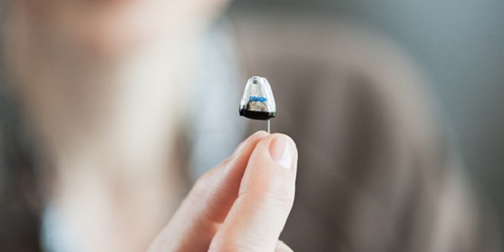 Kobieta trzyma dyskretny aparat słuchowy w Centrum Słuchu Audika.